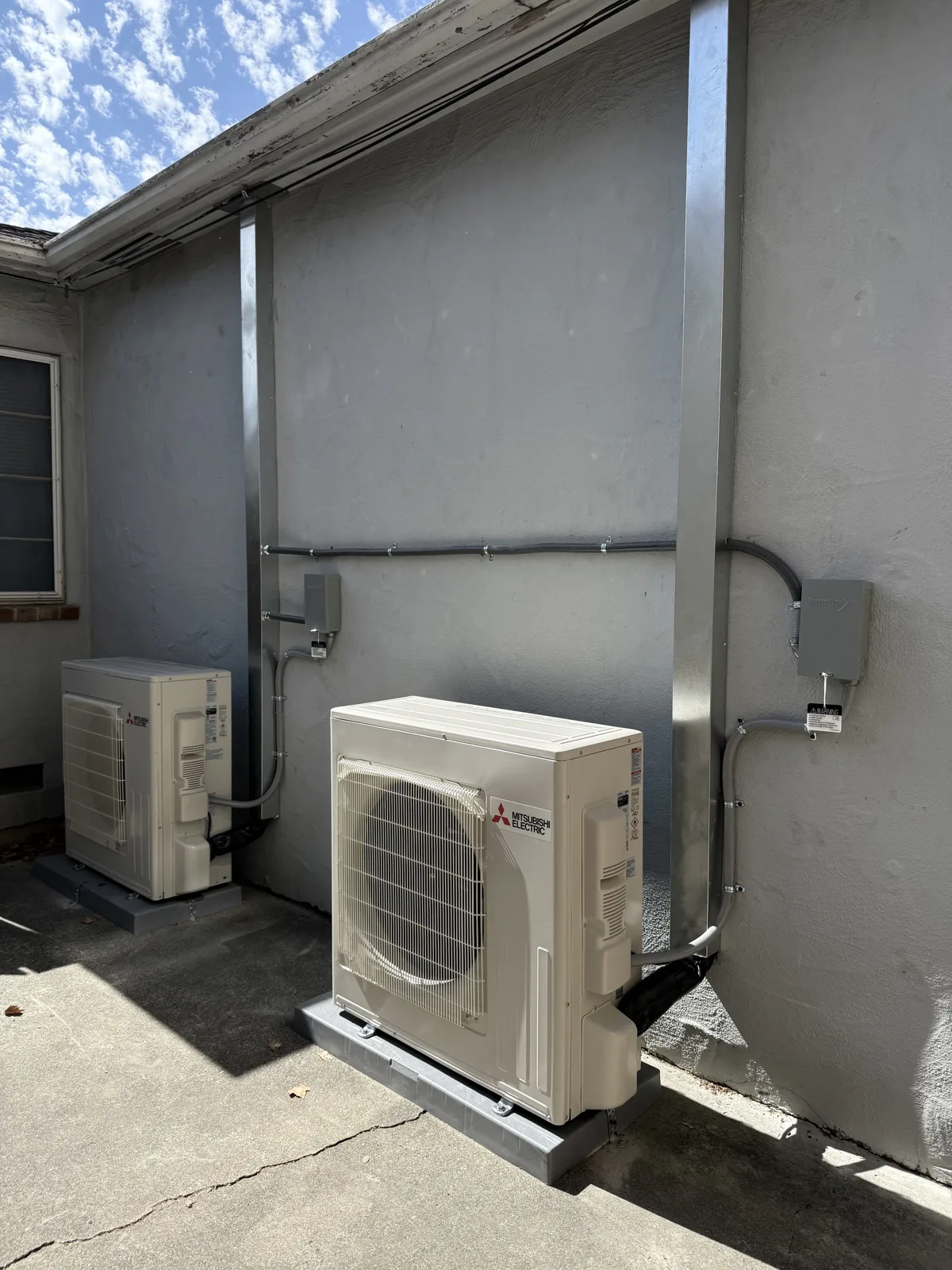 Twin Mitsubishi Electric heat pump condensers on custom pads with concealed line-set covers